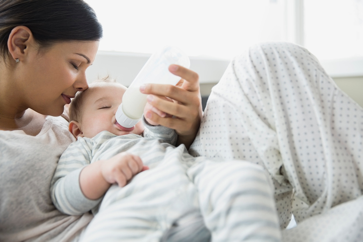 Woman checking temperature of infant formula at table indoors, closeup. Baby milk