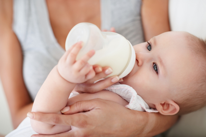 Woman checking temperature of infant formula at table indoors, closeup. Baby milk